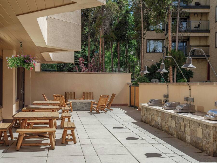 An outdoor patio with wooden tables and chairs, a stone wall, and outdoor lighting.