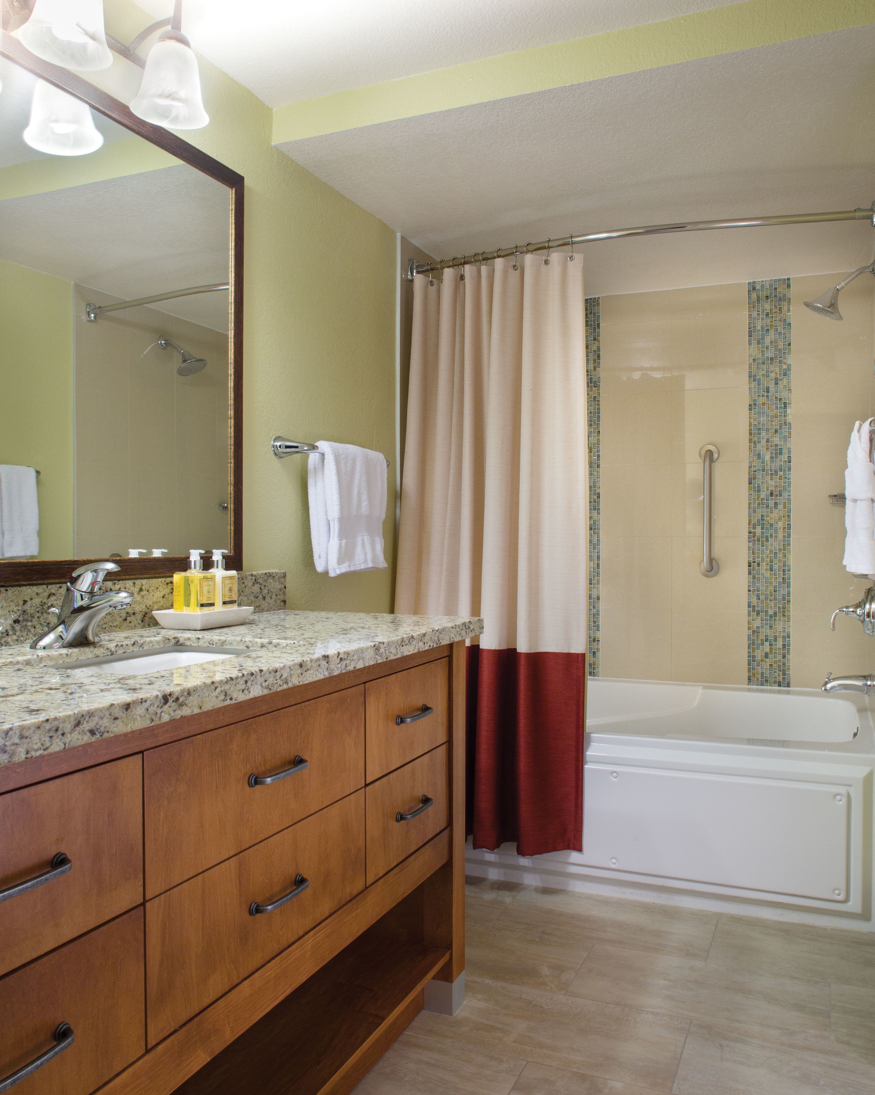 Une salle de bain dotée d’un comptoir en granit, d’un meuble-lavabo en bois, d’un grand miroir, d’une douche avec une porte en verre et d’une baignoire.