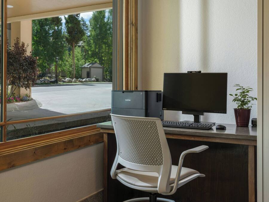 Een moderne kantoorruimte met een groot raam, een bureau met een computer en een witte stoel.