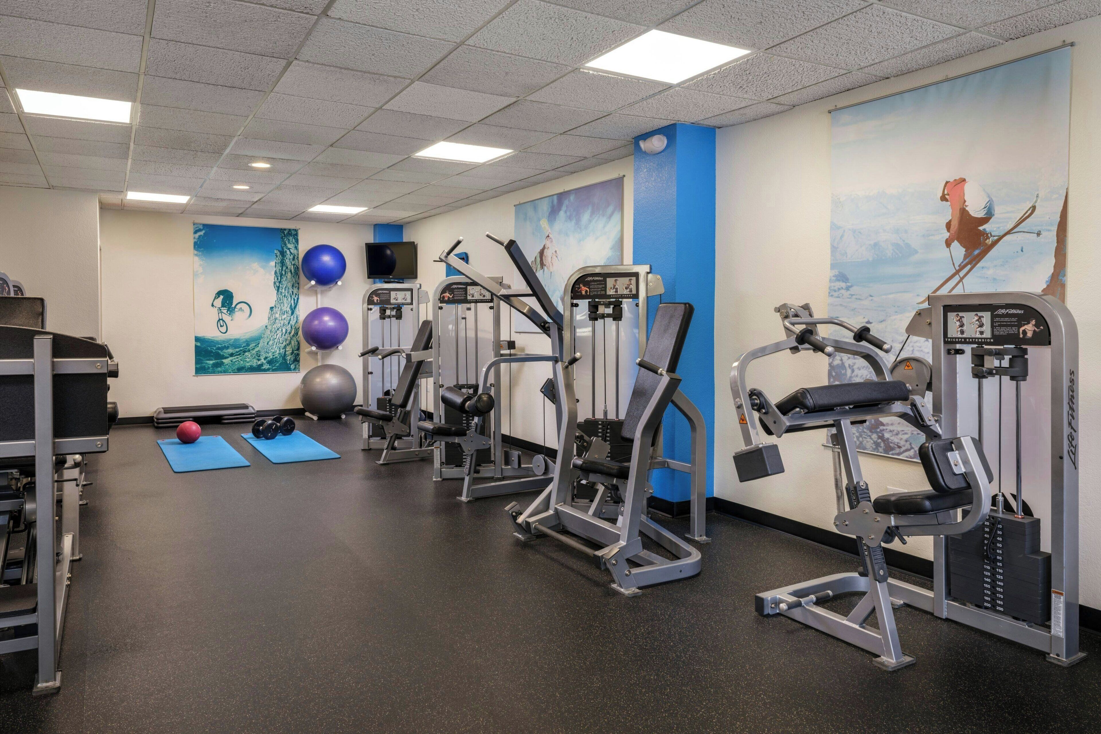 A gym with various exercise machines, blue mats, and fitness balls.