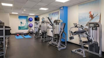 A gym with various exercise machines, blue mats, and fitness balls.