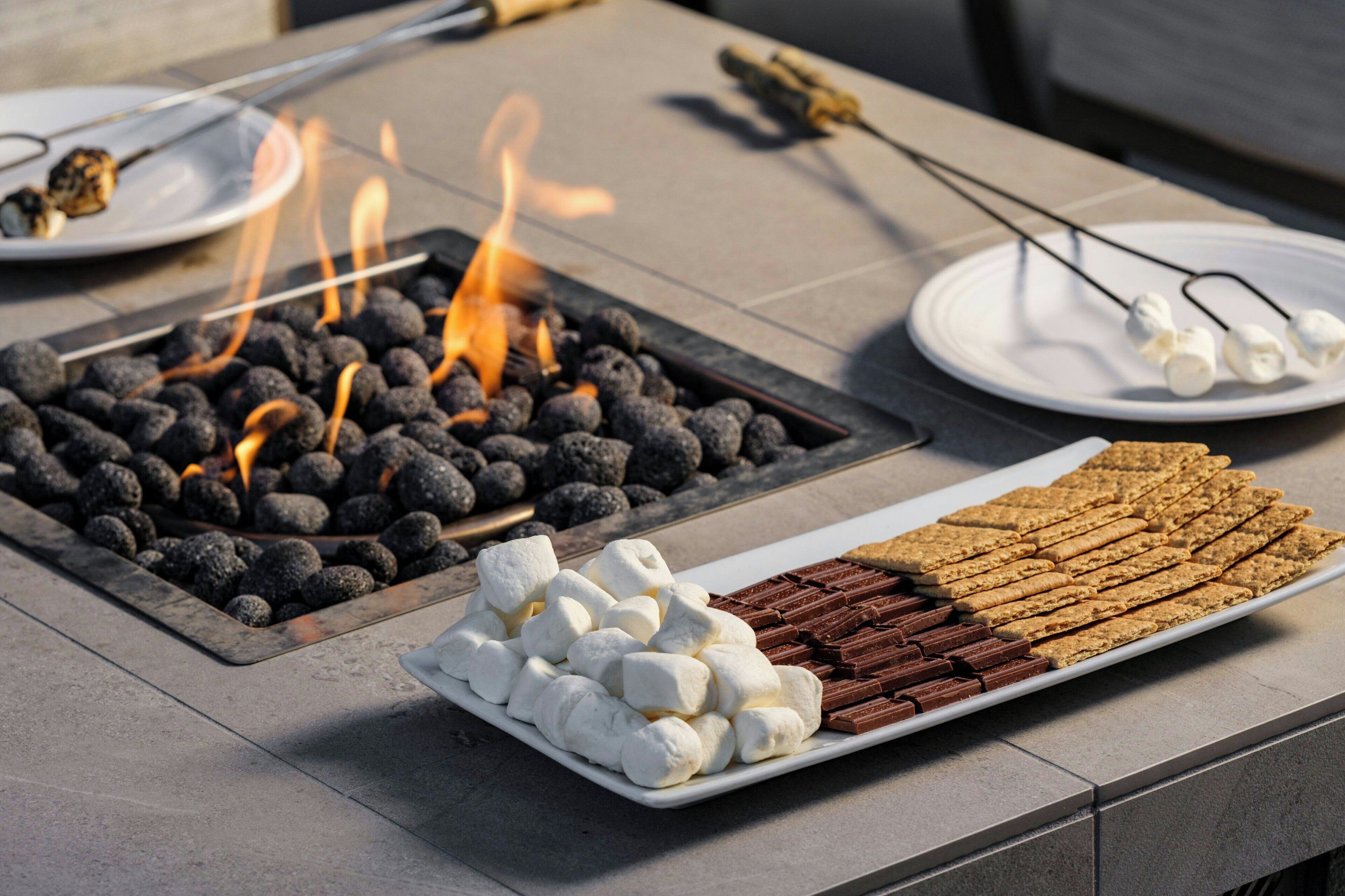 A table with a charcoal fire, marshmallows, and chocolate bars.