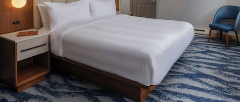 A hotel room with a large bed, a nightstand, a desk, a chair, and a door.