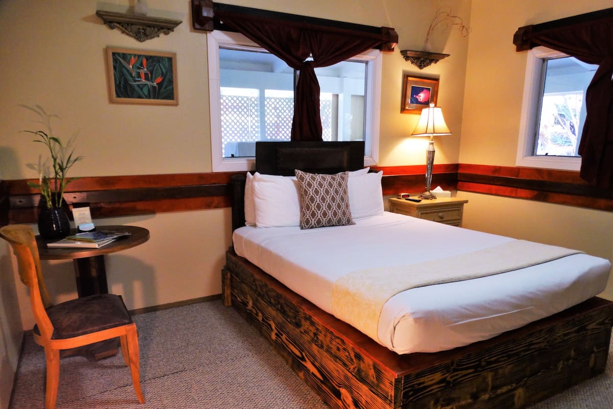 A neatly arranged hotel room with a large bed, a bedside table, a chair, and a window with curtains.