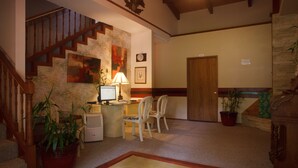 A living room with a staircase, a desk with a computer, two chairs, and several potted plants. - Lokahi Lodge (Volcano)