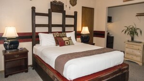 A neatly made bed with a wooden headboard, two bedside tables with lamps, a mirror, and a dresser with a plant. - Lokahi Lodge (Volcano)