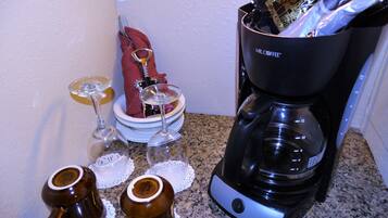 A kitchen with a coffee maker, two wine glasses, and two mugs on the counter.