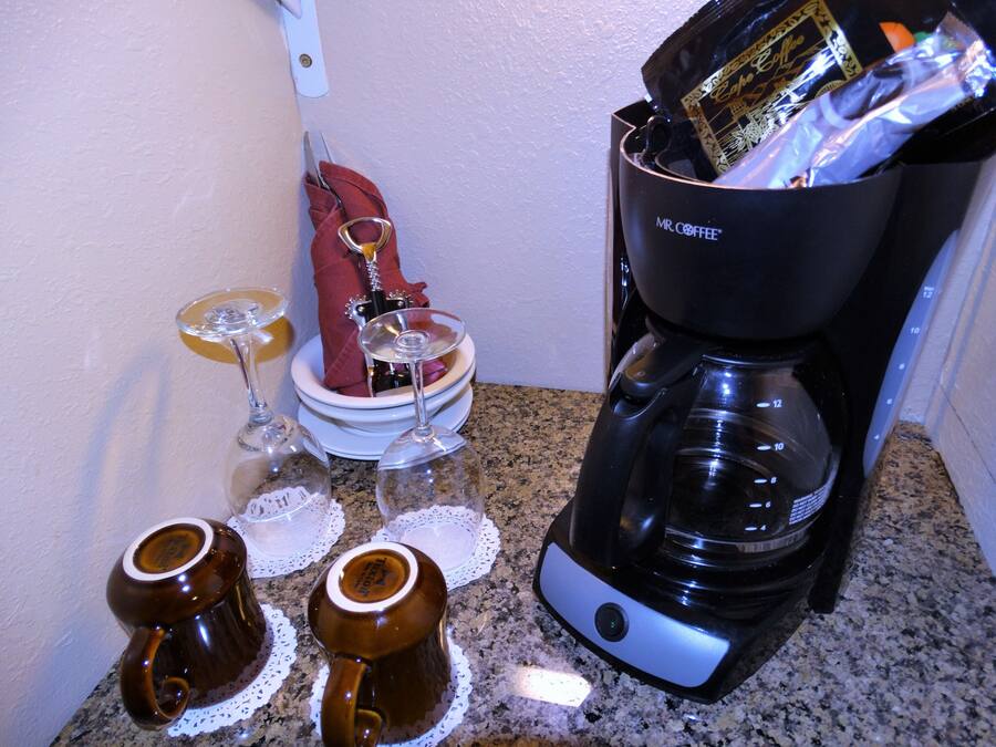 A kitchen with a coffee maker, two wine glasses, and two mugs on the counter.
