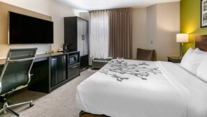 A hotel room with a bed, a desk with a chair, a television, a wardrobe, and a window with curtains.