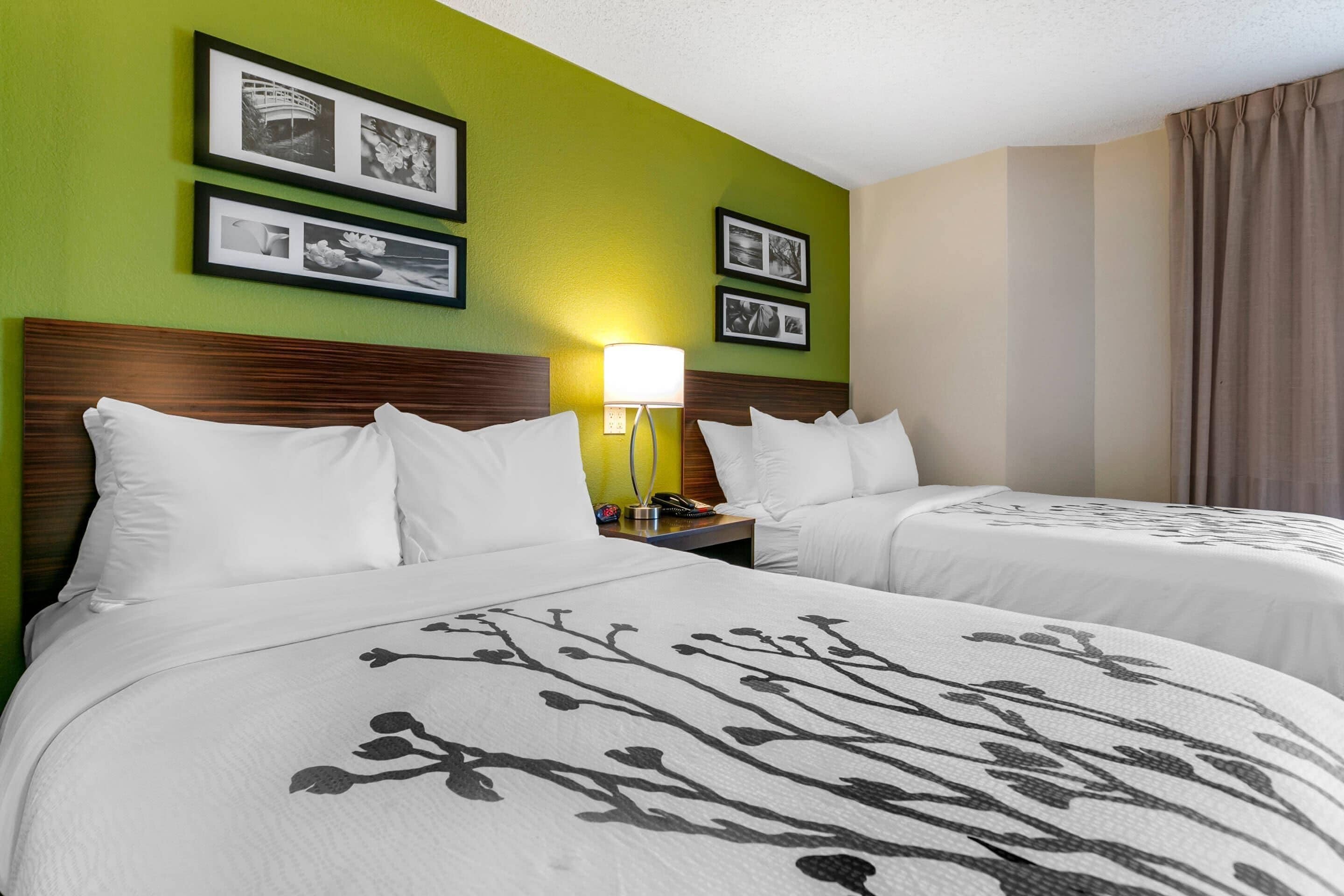 A hotel room with two beds, green walls, framed pictures, a bedside lamp, and a window with curtains.
