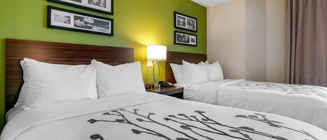 Habitación de hotel con dos camas, paredes verdes, cuadros enmarcados, una lámpara de noche y una ventana con cortinas.