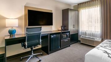Una habitación de hotel con cama, escritorio, computadora, televisor y mini refrigerador.