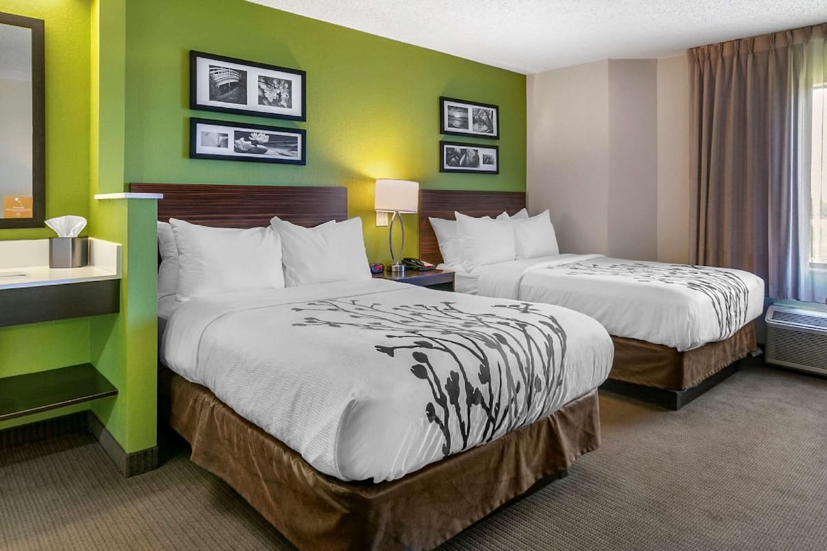 A hotel room with two beds, a bedside table with a lamp, a mirror, and framed pictures on the wall.