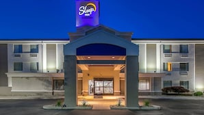 A Sleep Inn hotel entrance with a modern design, featuring a prominent sign, a covered entrance, and a landscaped area with plants.
