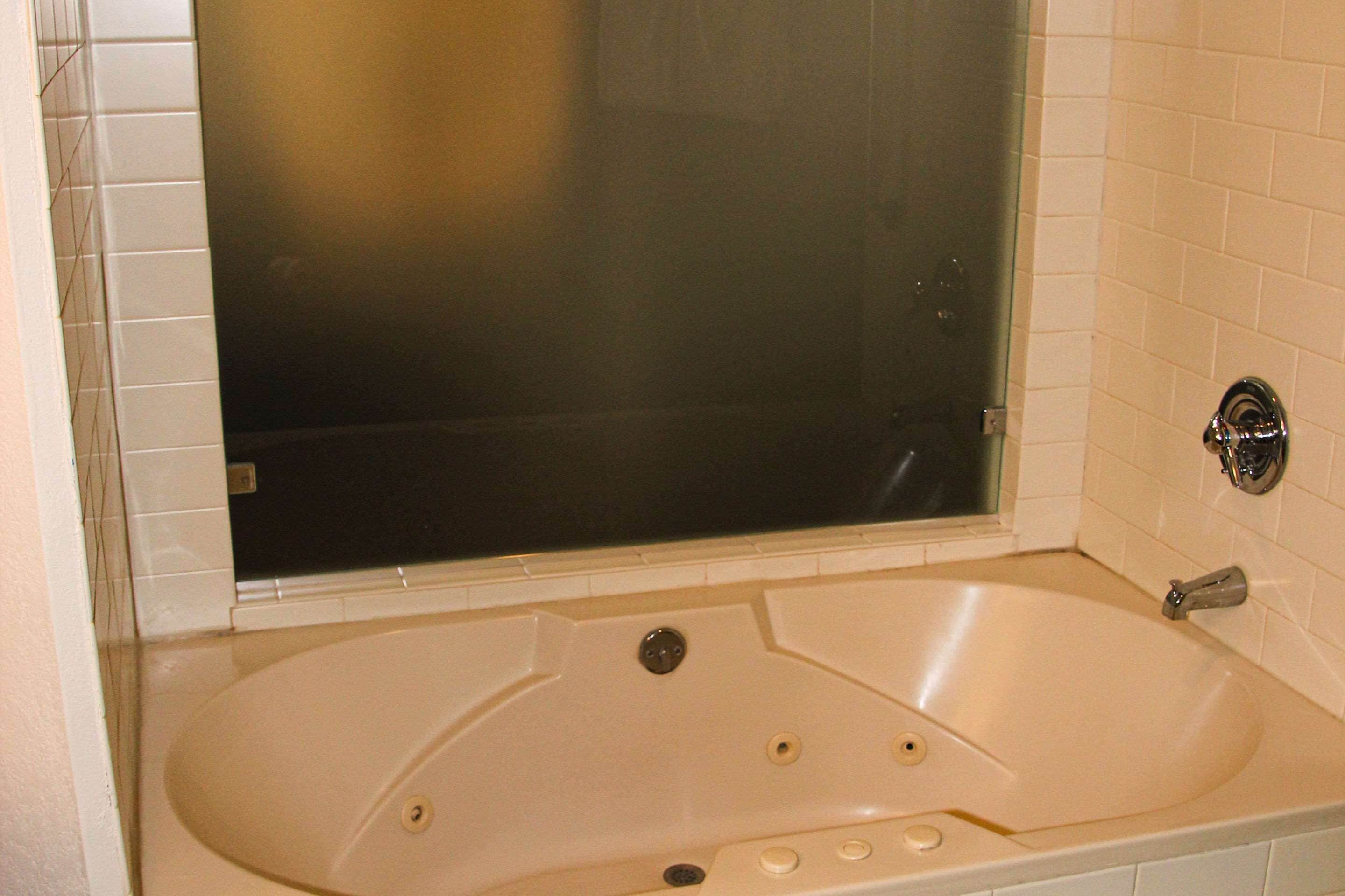 Une salle de bain avec une baignoire, un espace de douche vitré et un mur recouvert de carreaux blancs.