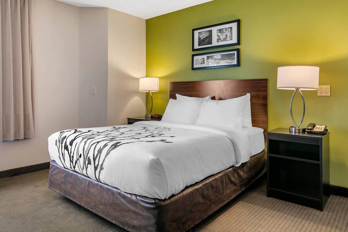 A hotel room with a large bed, two bedside tables with lamps, a wooden headboard, and green walls.