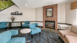 A modern lounge area with blue sofas, a fireplace, and a staircase with a green accent wall.
