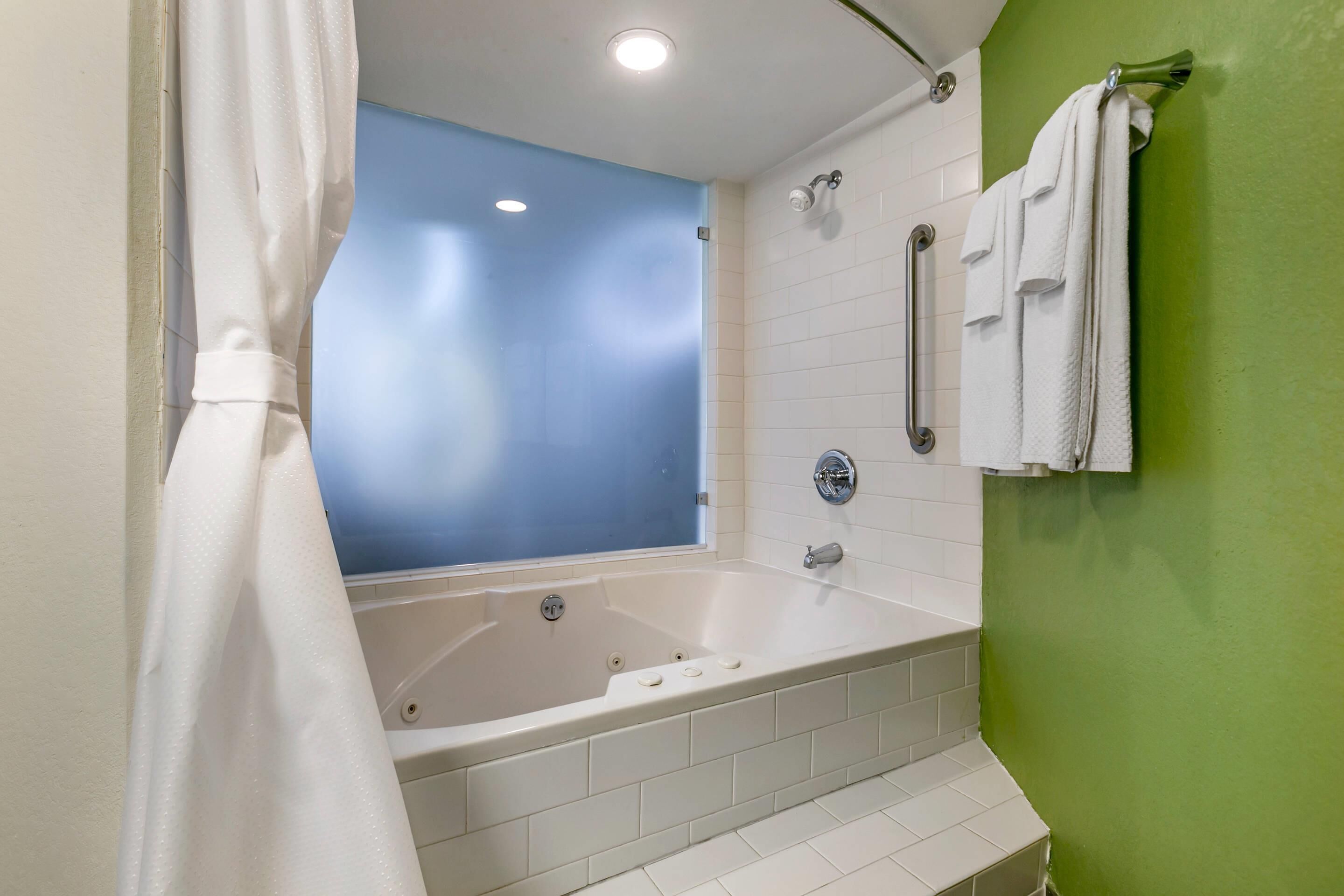 A modern bathroom with a large bathtub, a shower, and a green accent wall.