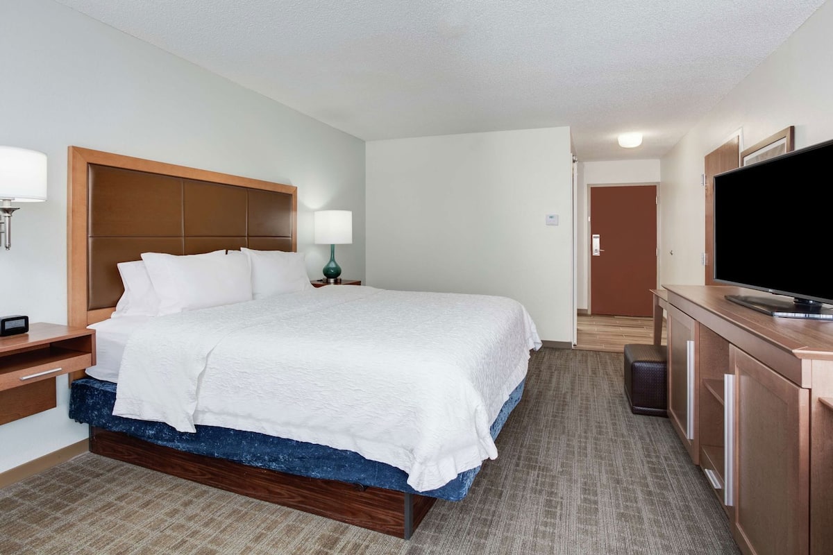A hotel room with a bed, bedside table, lamp, TV, and a door leading to another room.
