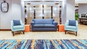 Eine Lobby mit einem blauen Sofa, zwei gemusterten Sesseln, einer Uhr und einem Teppich mit Muster.