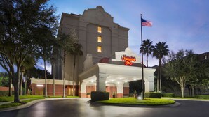 Ein Hampton Inn Hotel im klassischen Baustil, mit einem markanten Eingang, einer US-amerikanischen Flagge und gepflegter Bepflanzung.