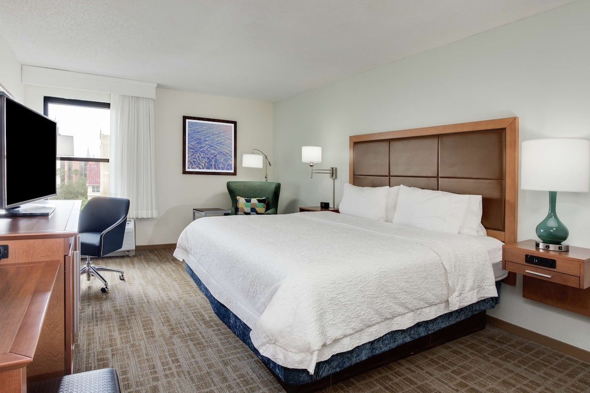 Une chambre d’hôtel avec un grand lit, un bureau avec une chaise, une télévision et une fenêtre avec des rideaux.