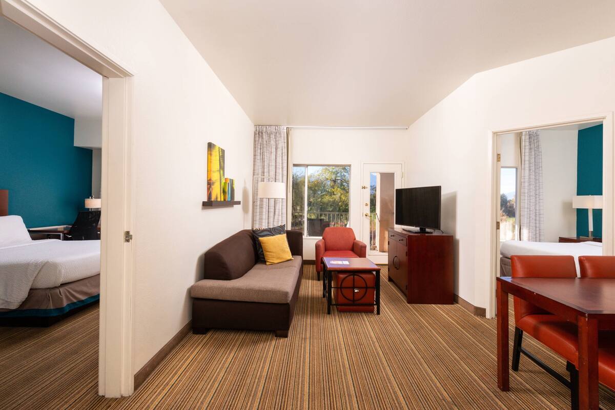 A hotel room with a bed, a sofa, a TV, a dining table, and a view of the outdoors.