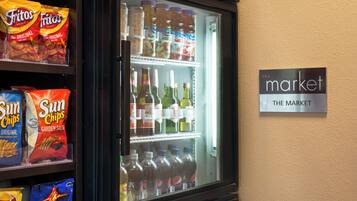 Un réfrigérateur rempli d’en-cas et de boissons, notamment des chips Fritos, Sun Chips et Doritos, avec une pancarte indiquant : « Le marché ».