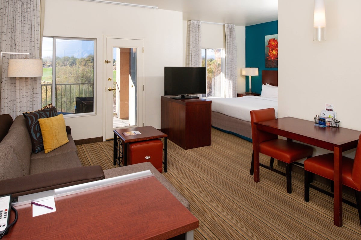 A hotel room with a bed, a TV, a desk, a chair, a sofa, and a window with a view of the outdoors.