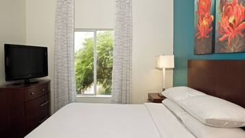Une chambre d’hôtel avec un lit, un téléviseur posé sur une commode en bois, une fenêtre avec des rideaux et un tableau accroché au mur.