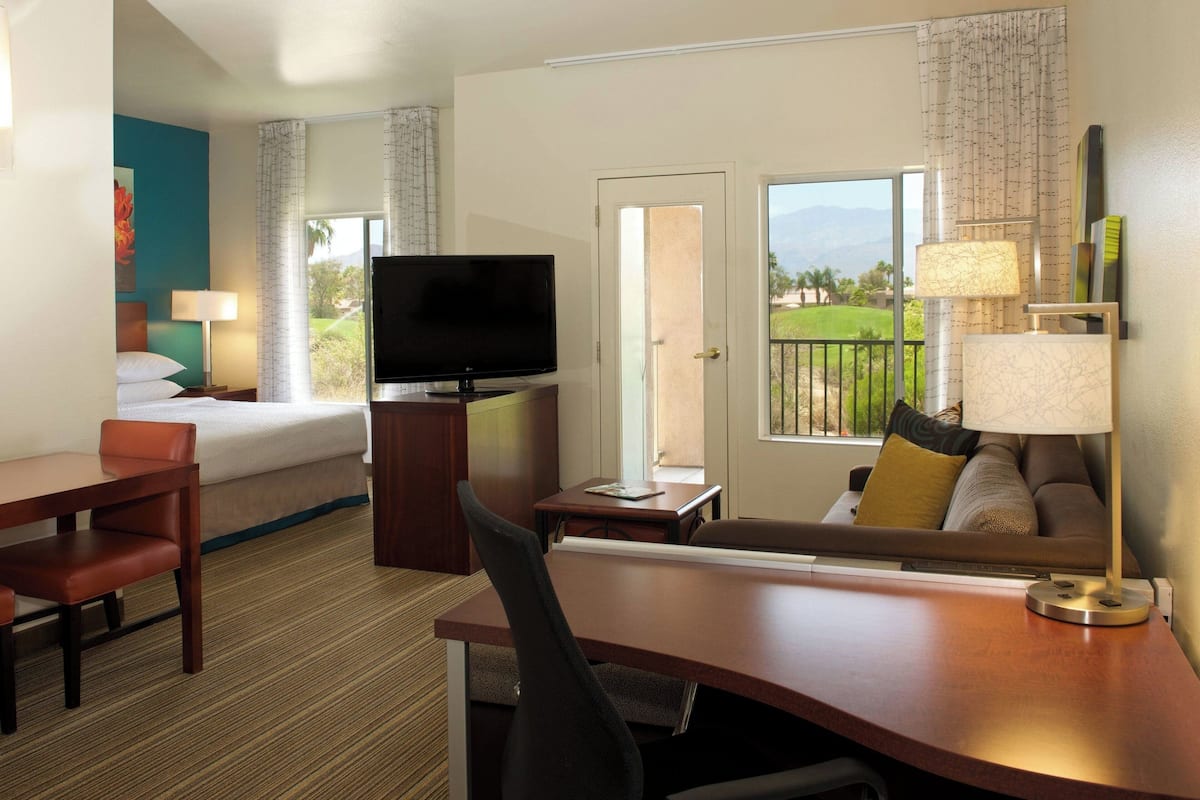 A hotel room with a bed, a desk, a television, a sofa, and a view of the outdoors.