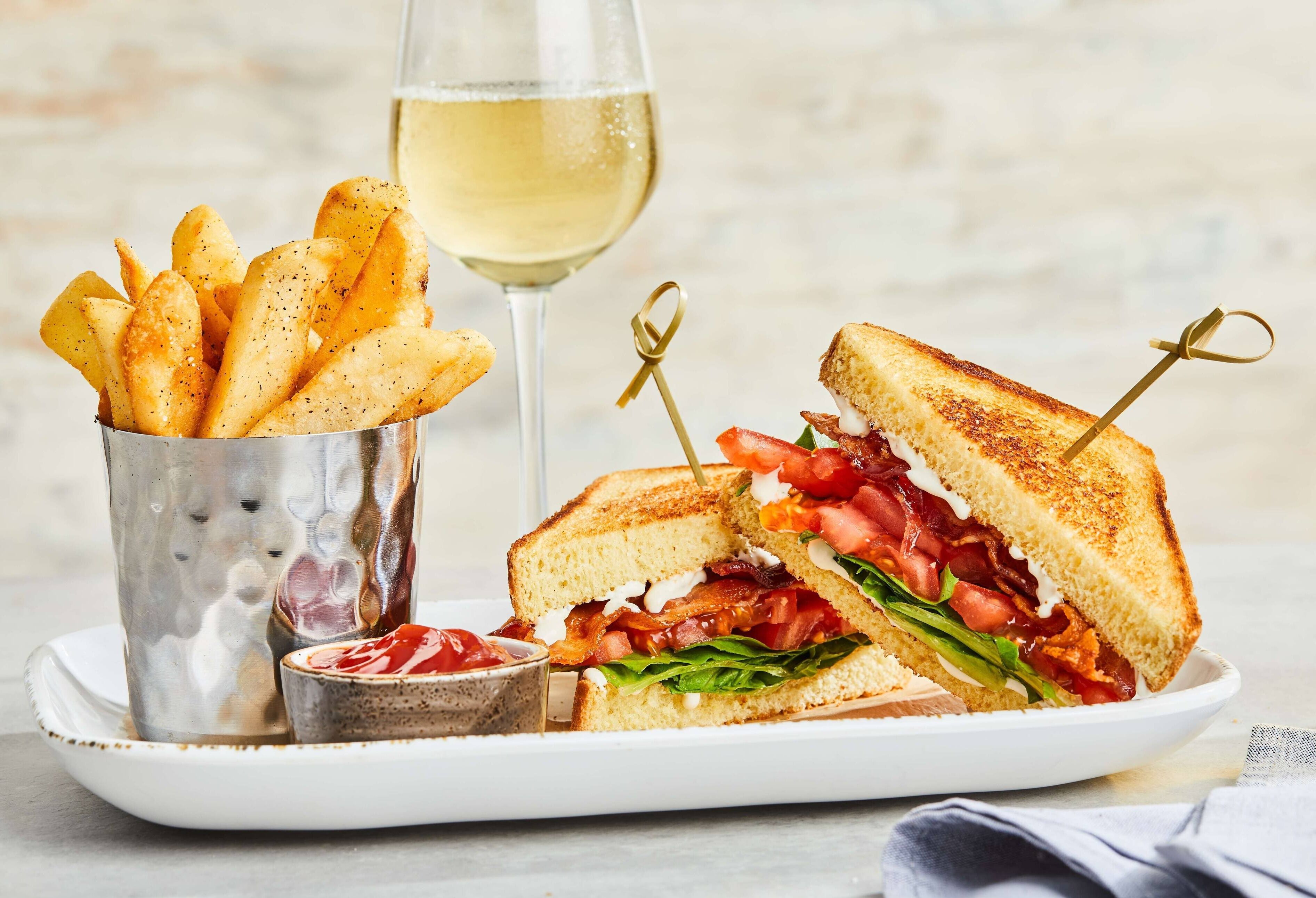 Une assiette avec un sandwich grillé, des frites et un verre de vin blanc.