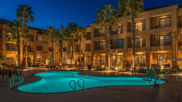 A hotel with a swimming pool surrounded by palm trees and lounge chairs. - Courtyard by Marriott Palm Desert (Palm Desert)
