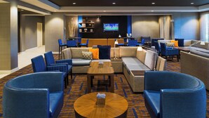 A modern hotel lobby with a seating area, a TV screen, and a wooden coffee table. - Courtyard by Marriott Palm Desert (Palm Desert)
