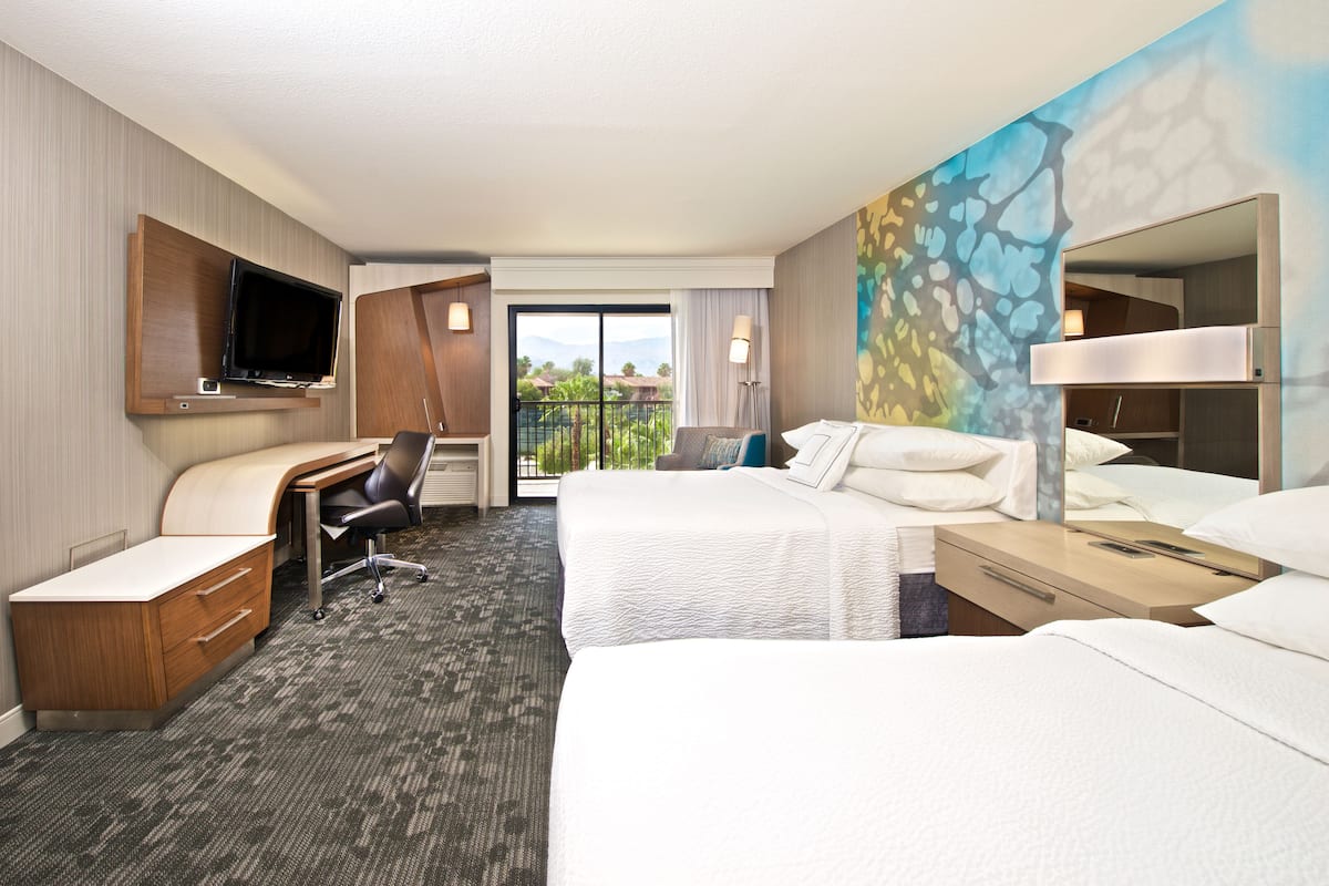 A hotel room with two beds, a desk, a TV, and a balcony with a view.