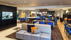 A modern hotel lobby with a seating area, a bar, and a television displaying a news channel. - Courtyard by Marriott Palm Desert (Palm Desert)