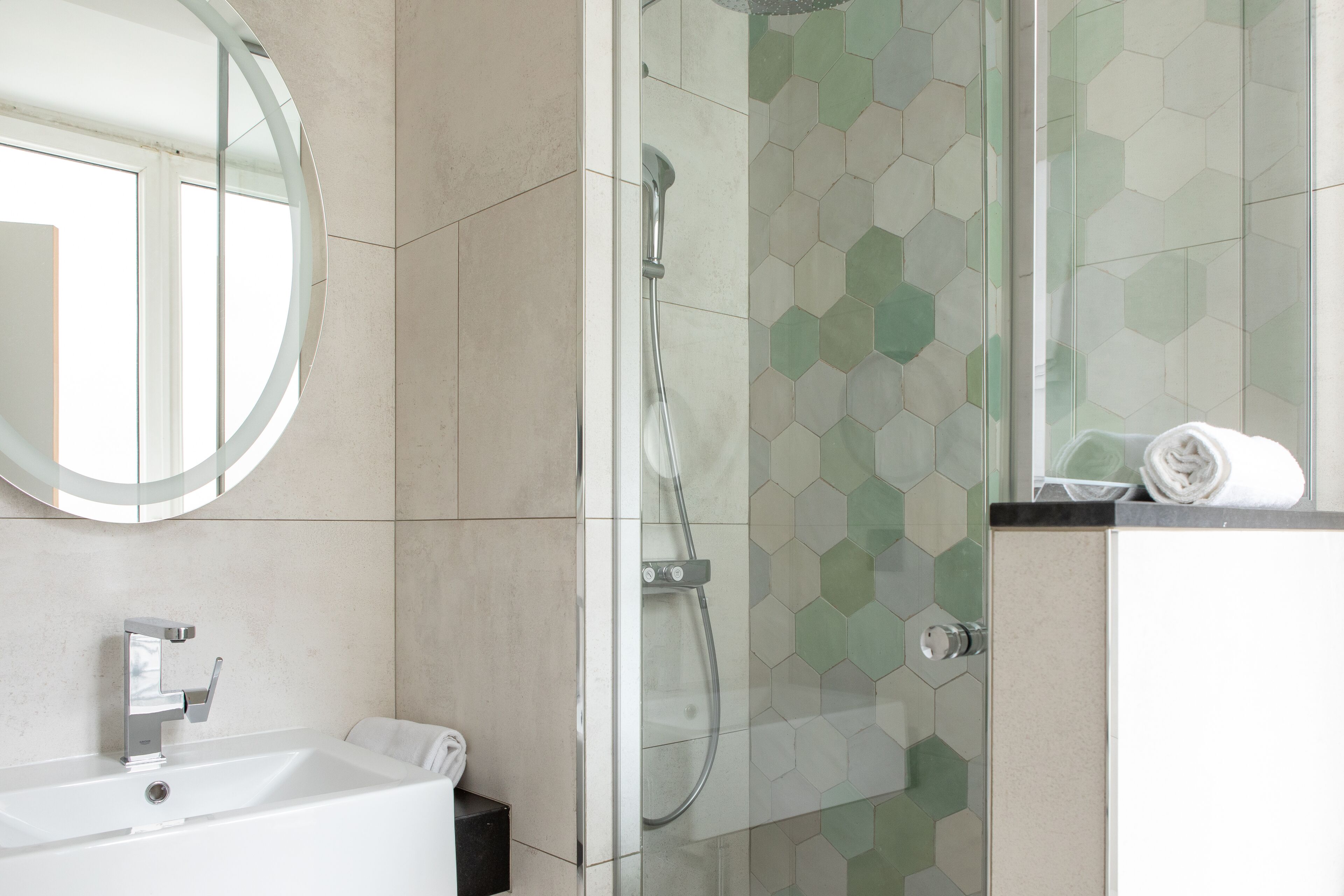 Un baño moderno con cabina de ducha de vidrio, un espejo redondo y un lavabo blanco.