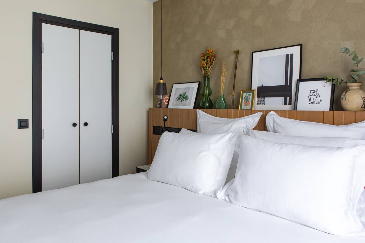 Una habitación de hotel con una cama, una mesita de noche de madera, un espejo y una pared decorada con cuadros y un florero.
