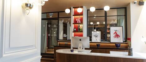 A reception area with a wooden reception desk, a large Apple iMac computer, and a red shelf with various items.