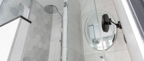 Un baño moderno con cabina de ducha de vidrio, un espejo redondo y un lavabo blanco.