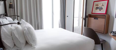 Una habitación de hotel con cama, escritorio, silla, lámpara de escritorio, un marco de fotos y una ventana con cortinas.