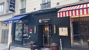 A hotel named Maison Mère with a black facade, a red and white striped awning, and a sign indicating it is a cocktail bar. - Maison Mère (Paris)