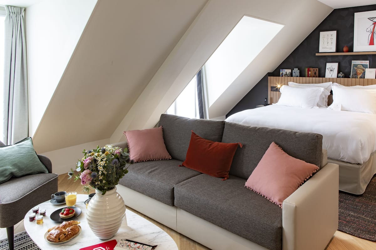 Un dormitorio tipo loft moderno con una cama grande, un sofá gris y un comedor con desayuno.
