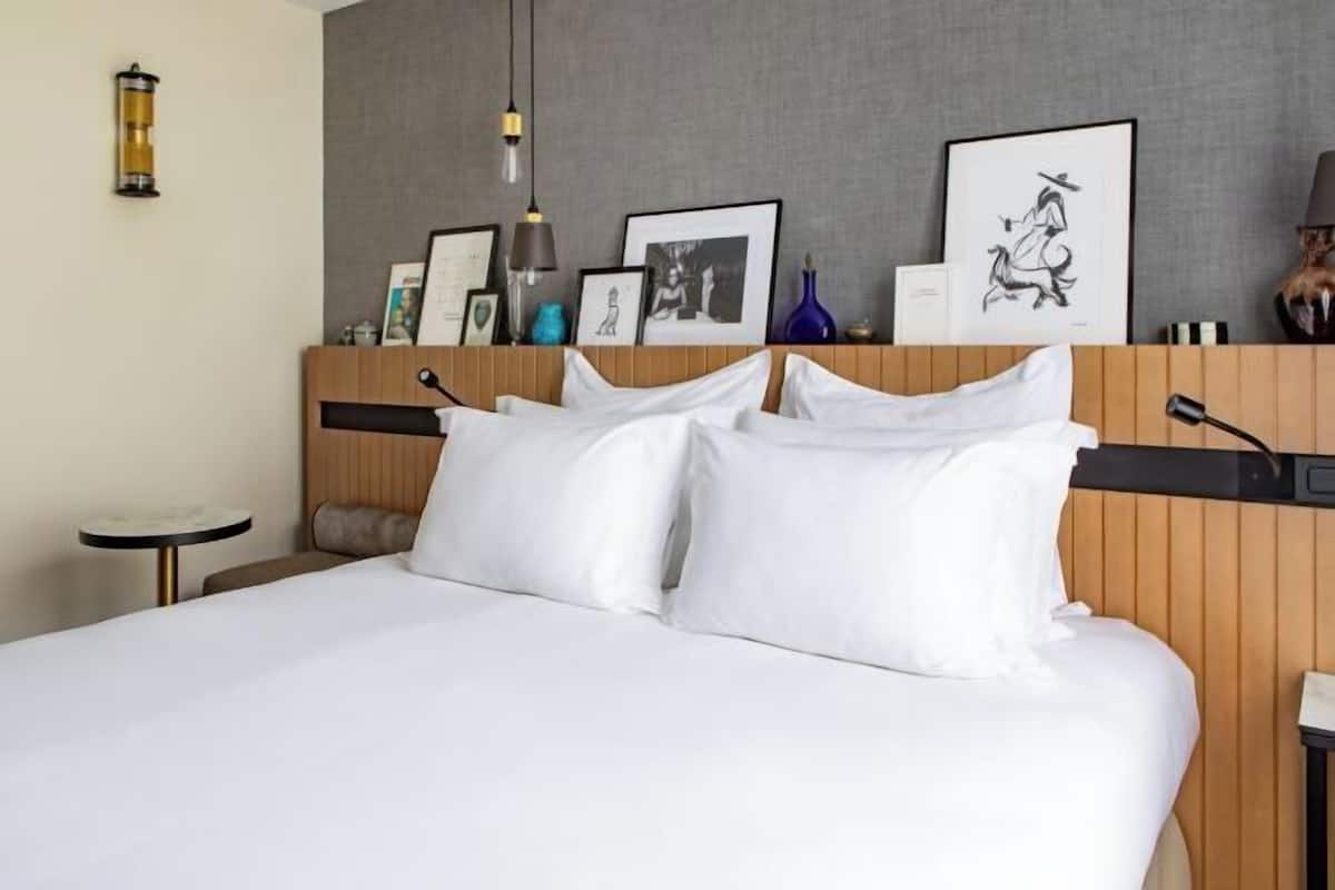 Habitación de hotel con cama, una mesita redonda, una lámpara y cuadros en la pared.