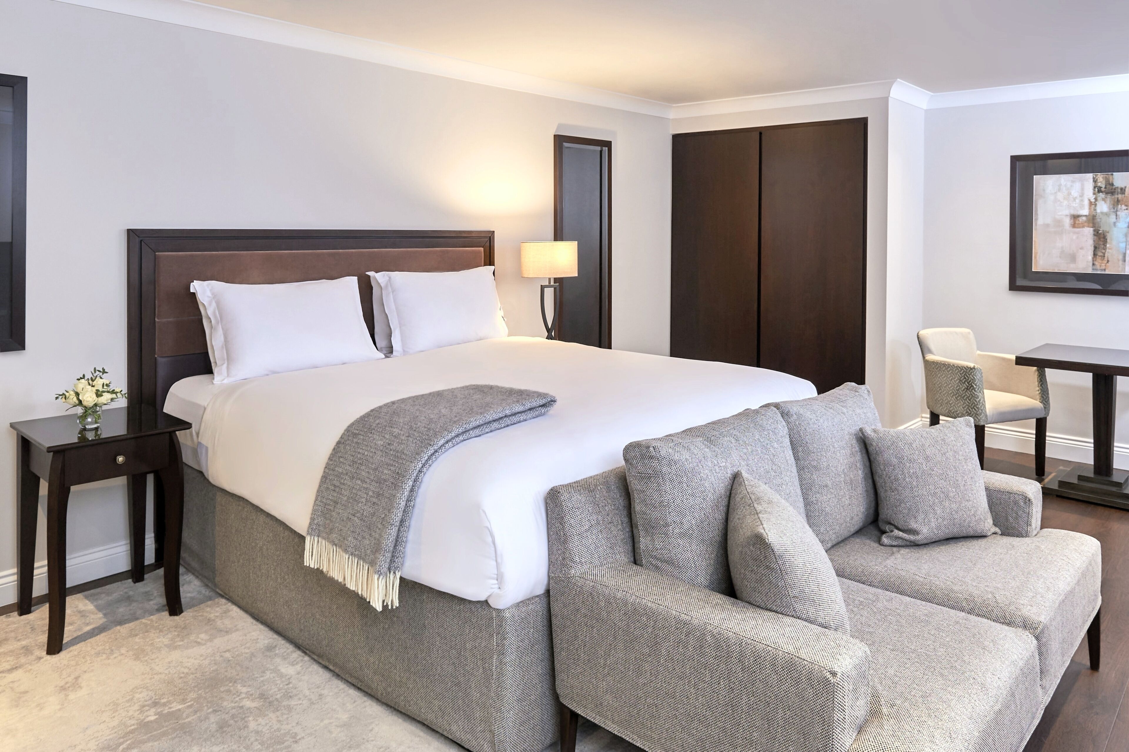 Een hotelkamer met een groot bed, een grijze bank, een kleine tafel en een stoel.