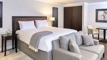 A hotel room with a large bed, a grey sofa, a small table, and a chair.