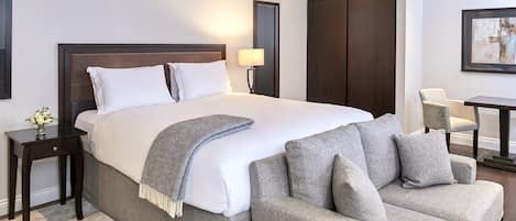 A hotel room with a large bed, a grey sofa, a small table, and a chair.