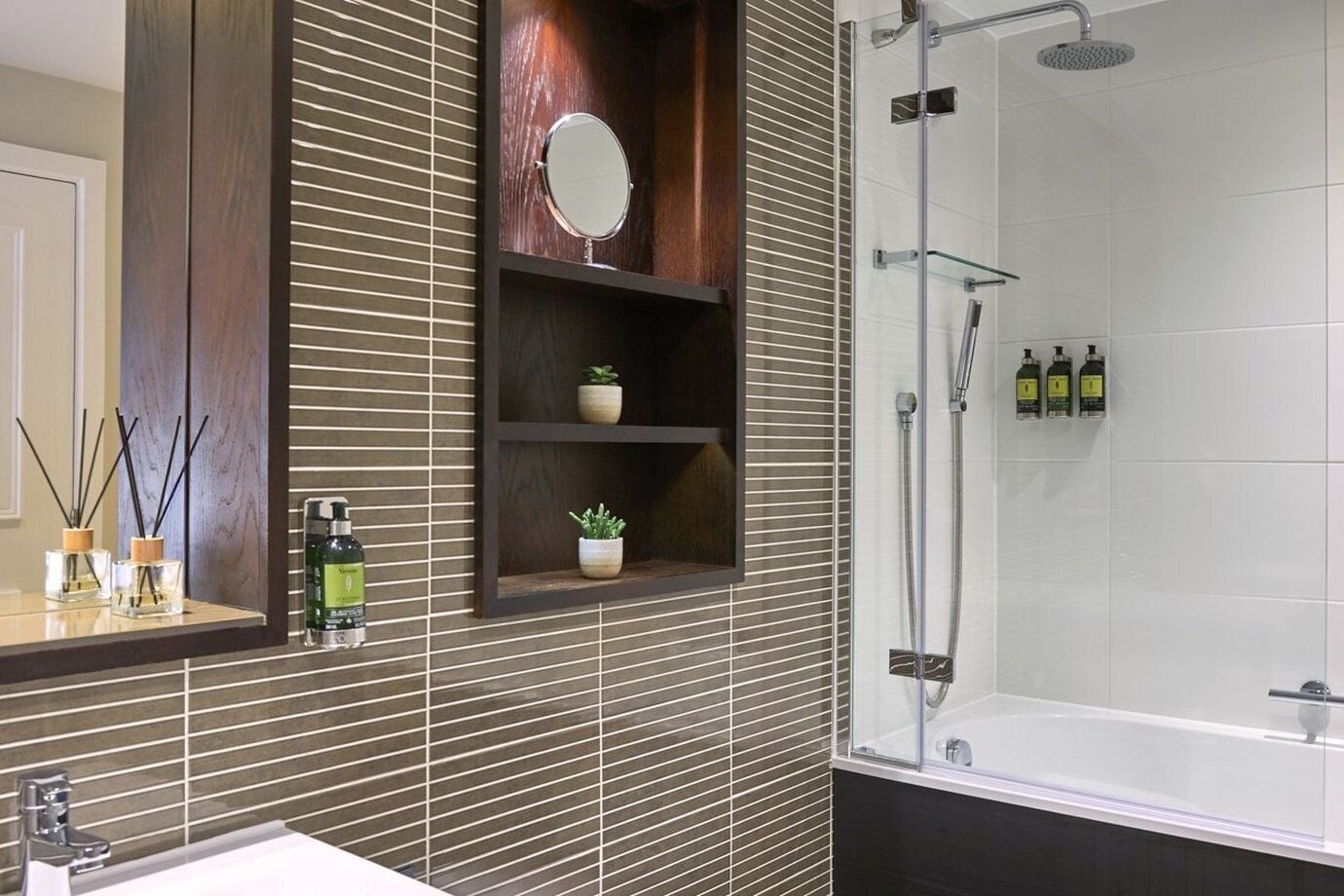 Een moderne badkamer met een grote spiegel, een douche met glazen wanden en een plank met toiletartikelen.