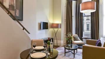 A dining area with a table set for two, a sofa, and a TV mounted on the wall.