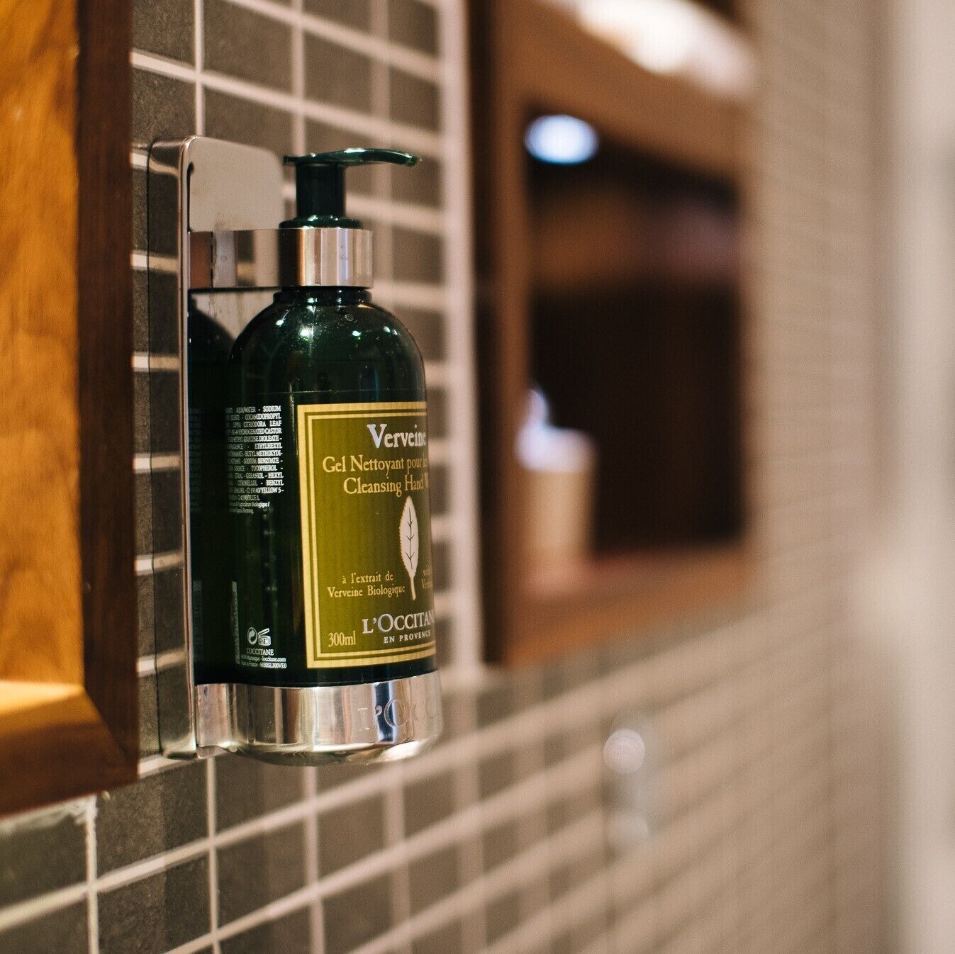 A bottle of Verveine cleansing hand gel mounted on a tiled wall.